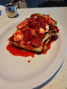 A plate of french toast with strawberries and whipped cream.