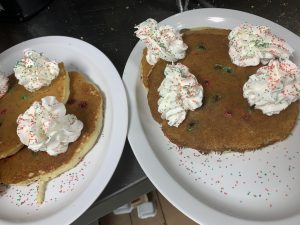 Two plates of pancakes with whipped cream on them.